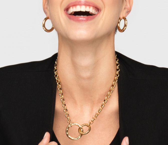 A person with large gold earrings and a gold chain necklace with two interlocking rings